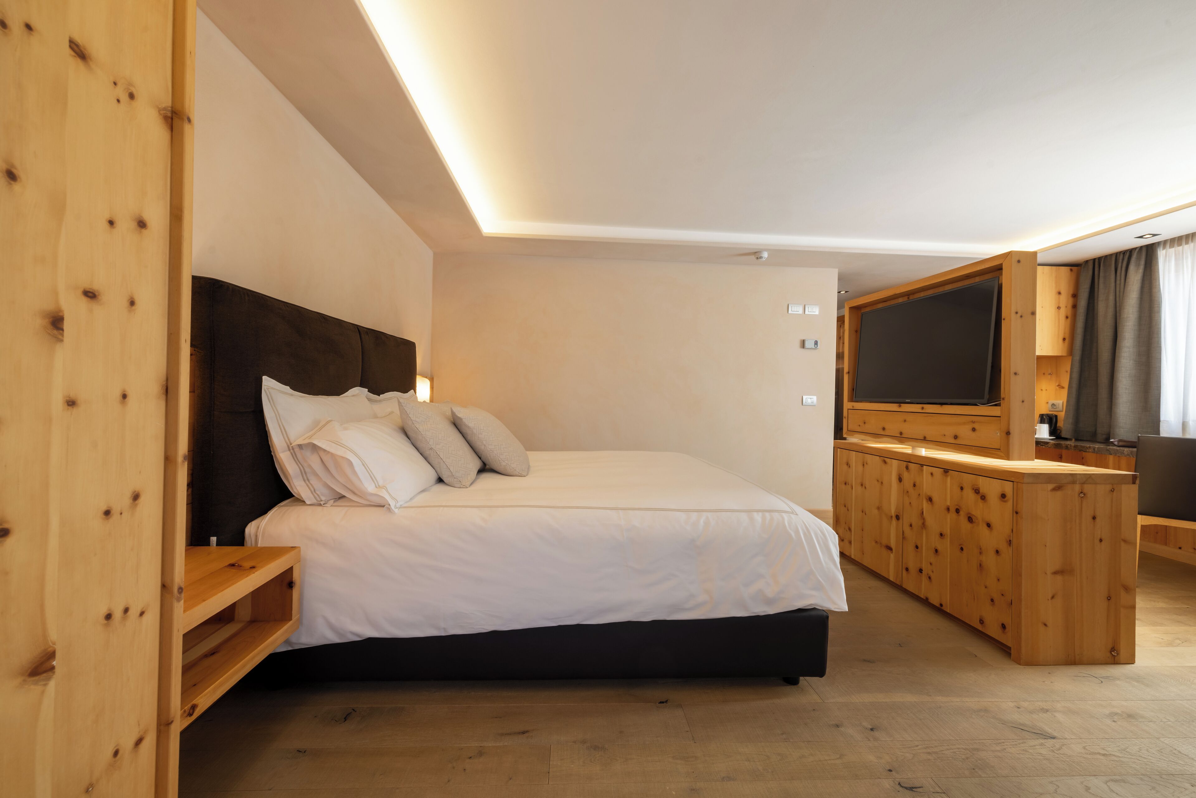 Un dormitorio con cama, cabecera de madera, mesitas de noche, televisor y un armario de madera.