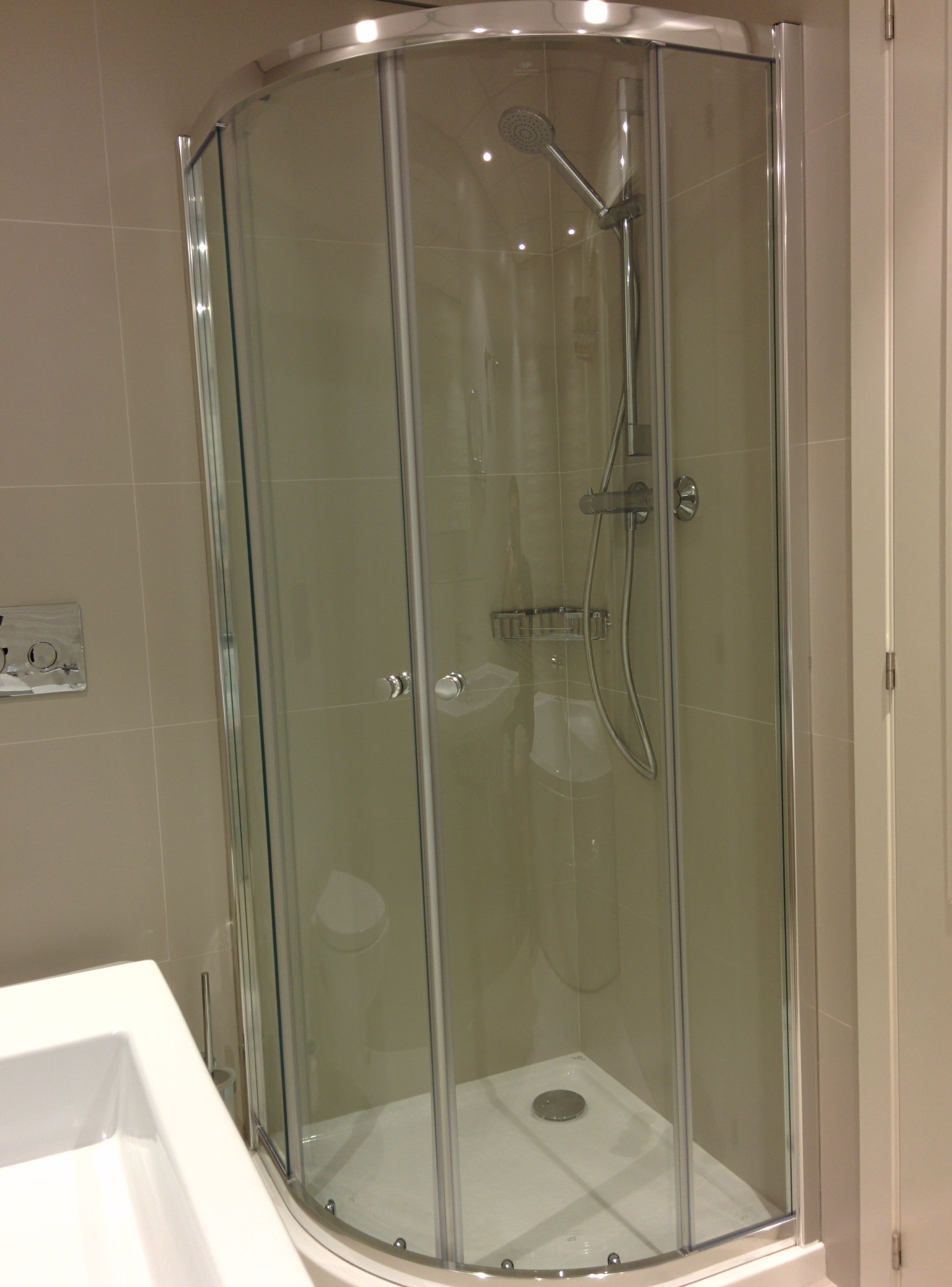 A glass-enclosed shower stall with a handheld showerhead and a wall-mounted faucet.