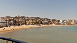 Vista costera con una playa despejada, edificios al fondo y una barandilla metálica al frente.