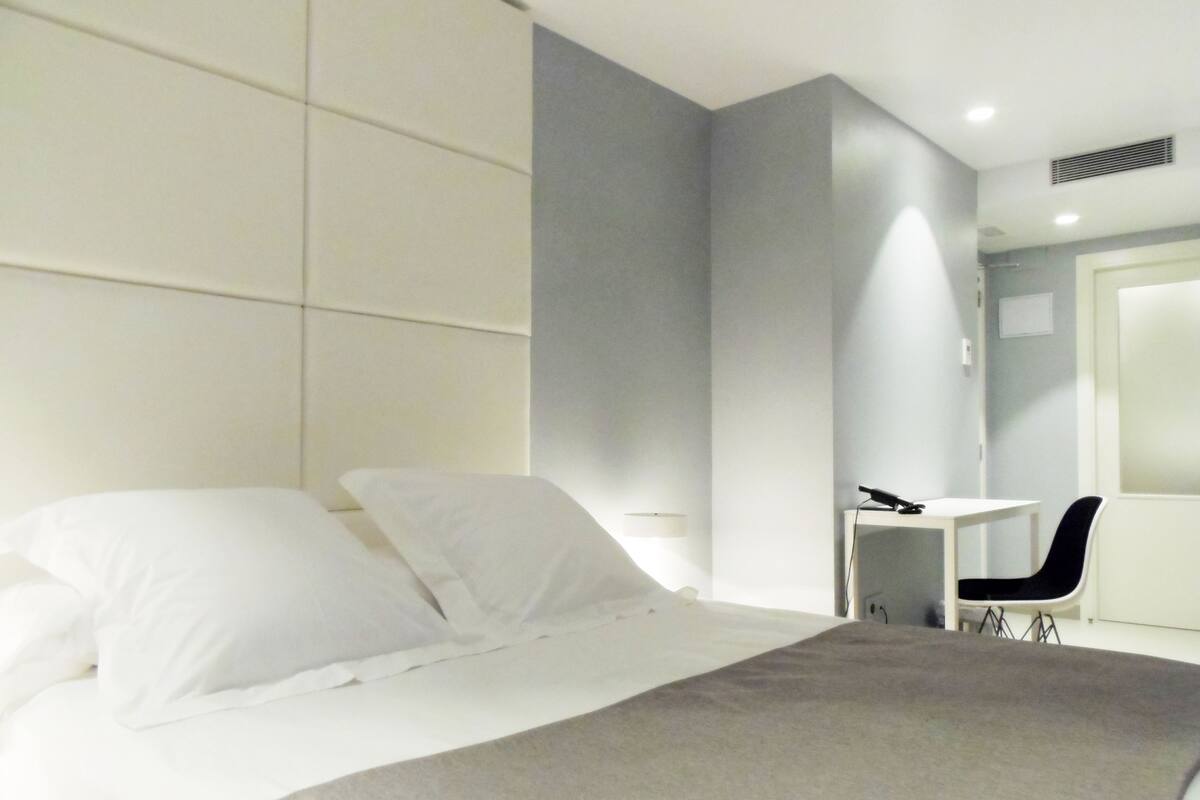 A modern hotel room with a large bed, a desk, and a chair.