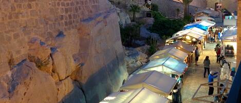 A historic stone wall with a market street lined with tents and people.