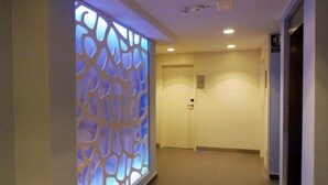 Un pasillo con un revestimiento mural decorativo de patrón geométrico, una puerta cerrada y un suelo de baldosas.