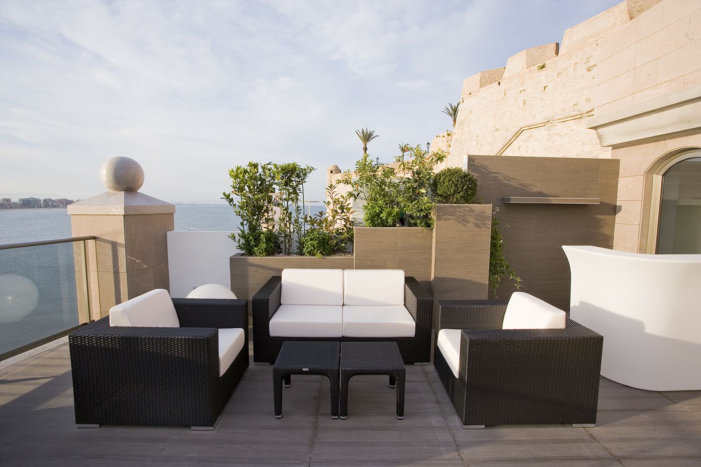 Una terraza en la azotea con mobiliario de mimbre, vista al mar y un muro de piedra.