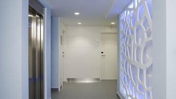 Un pasillo moderno con un ascensor metálico, luces empotradas en el techo y un panel decorativo en la pared.