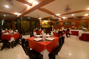 A restaurant with multiple tables set for dining, featuring red tablecloths and white napkins.
