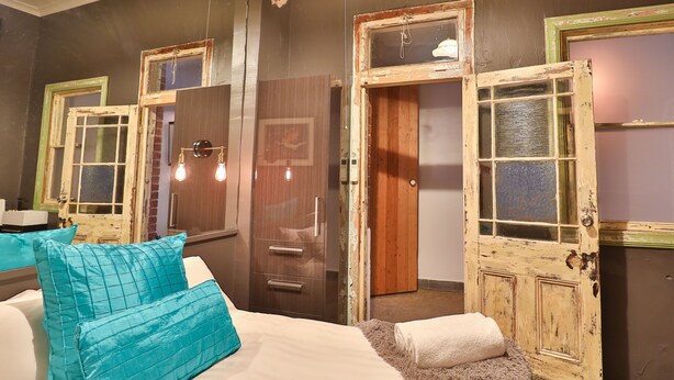 Un dormitorio con cama, almohadas color turquesa, cómoda y puerta de diseño rústico.