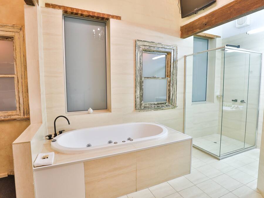 Un baño con una bañera independiente, cabina de ducha de vidrio y dos espejos con marcos envejecidos.
