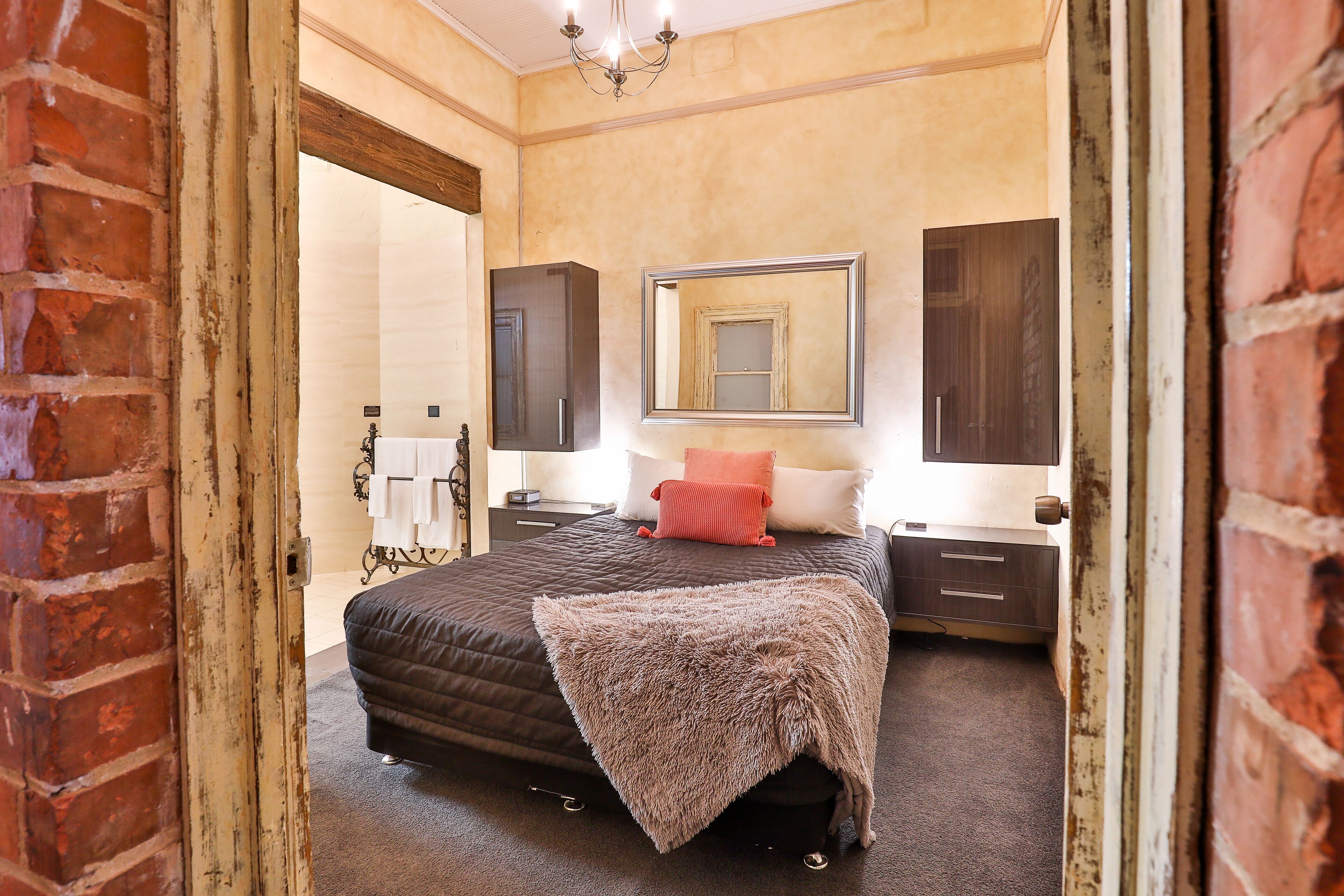 A bedroom with a large bed, a mirror, a dresser, and a brick wall.