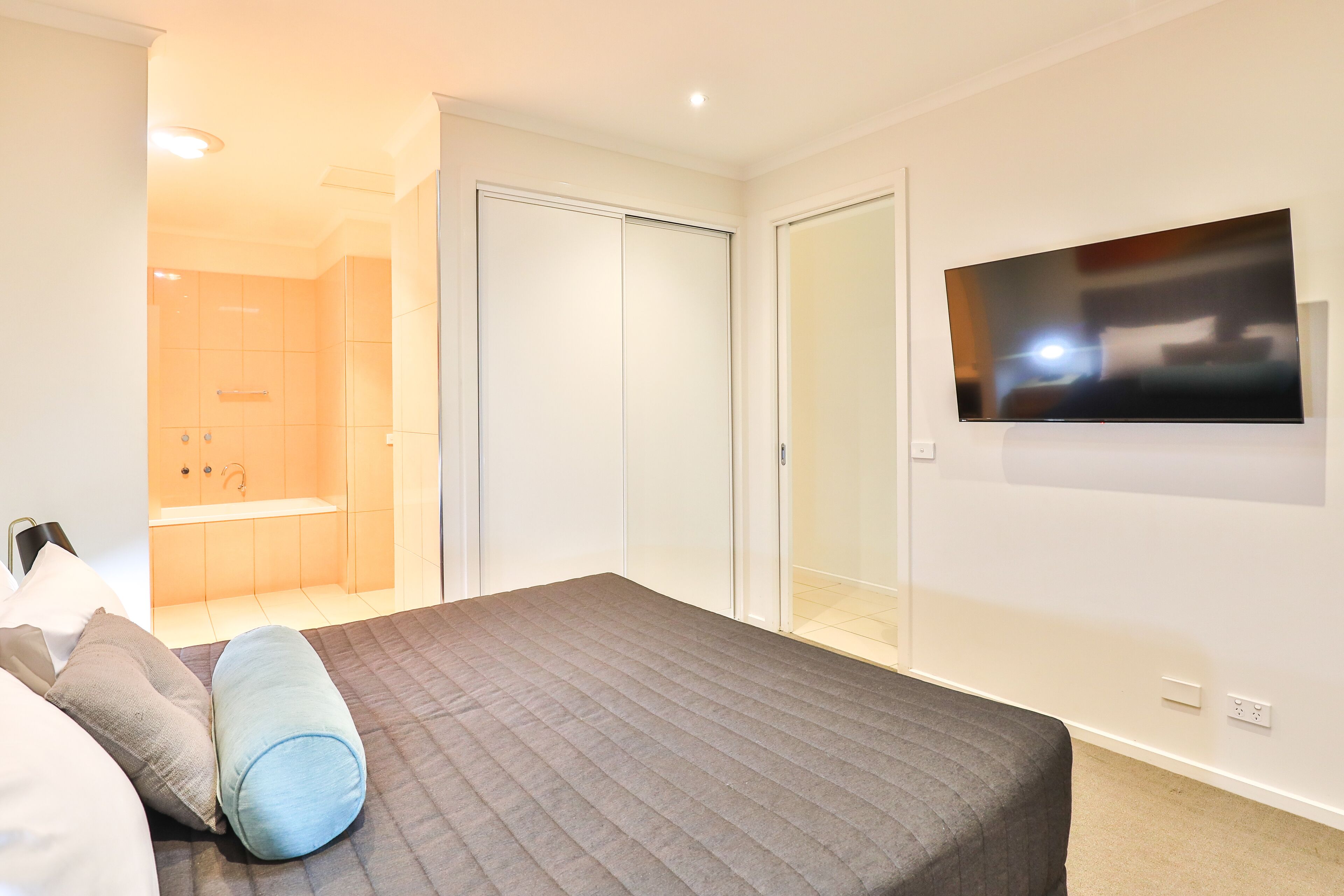 Un dormitorio con cama, televisor montado en la pared, vestidor y baño con ducha y lavamanos.