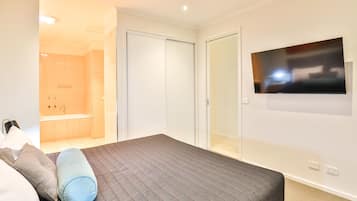 Un dormitorio con cama, televisor montado en la pared, vestidor y baño con ducha y lavamanos.