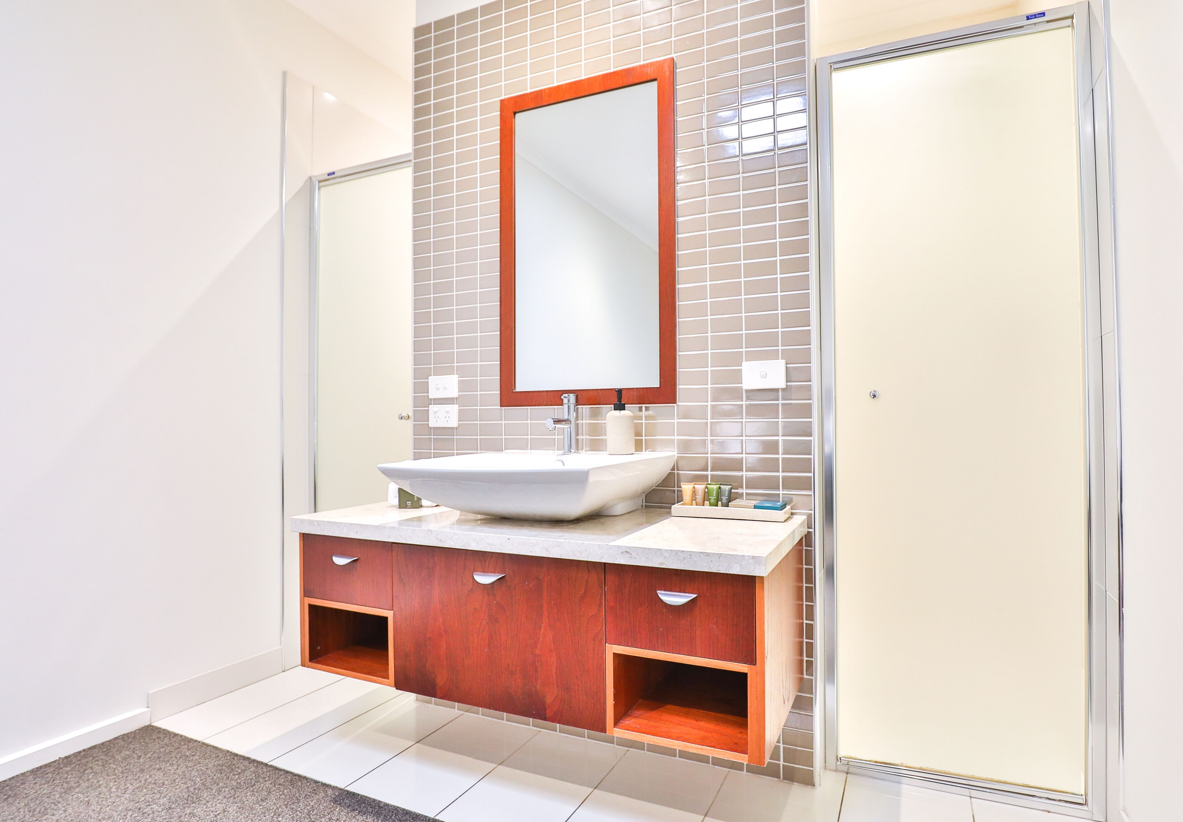 A modern bathroom with a large mirror, a white sink, wooden cabinets, and a shower area.
