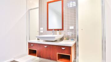 A modern bathroom with a large mirror, a white sink, wooden cabinets, and a shower area.