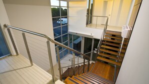 Un interior moderno con una escalera de madera, barandales de metal y ventanas amplias que ofrecen vistas al exterior.