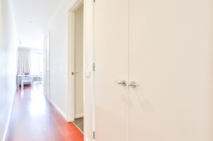 Un pasillo con suelo de madera, una puerta blanca y una mesa con sillas al fondo.