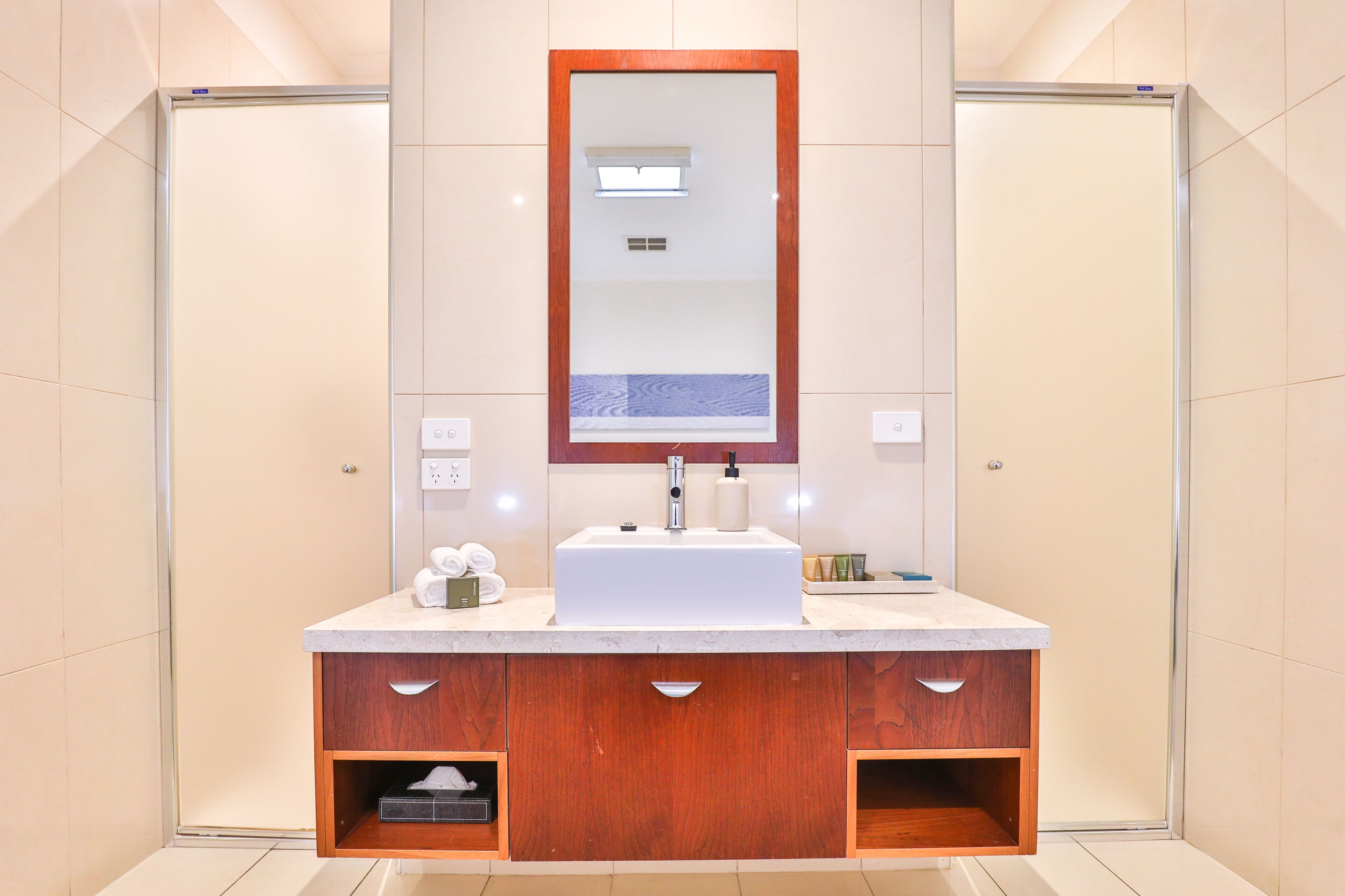 A modern bathroom with a large mirror, a white sink, and wooden cabinetry.