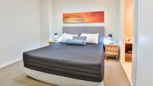 Un dormitorio moderno con una cama grande, un cabecero, dos mesitas de noche con lámparas y un cuadro abstracto colgado en la pared.