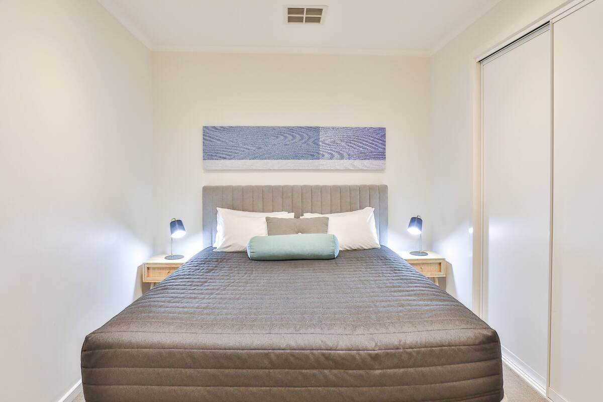 A neatly arranged bedroom with a large bed, two bedside tables with lamps, a headboard, and a wall-mounted artwork.