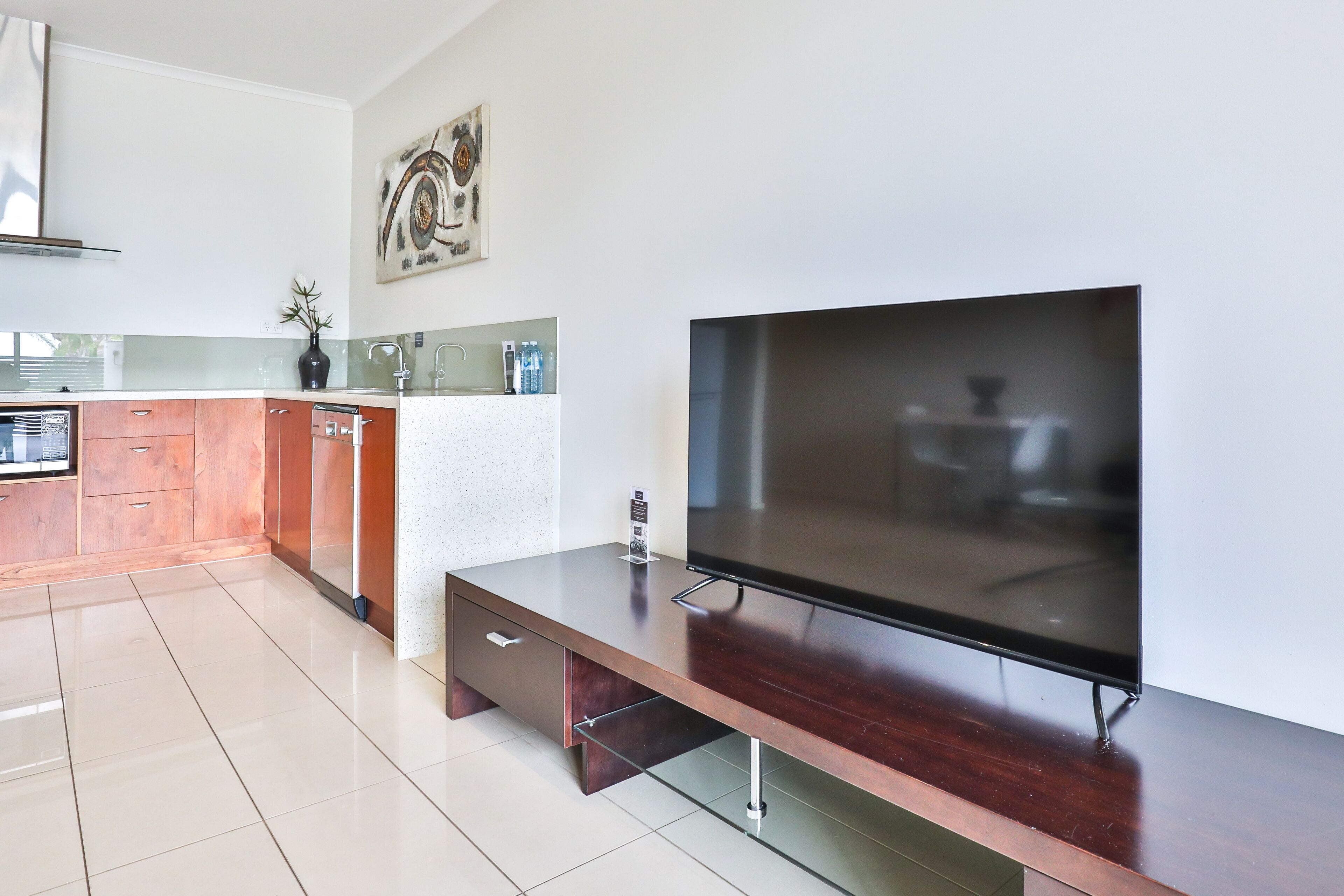 A modern kitchen with a flat-screen TV, wooden cabinets, and a tiled floor.