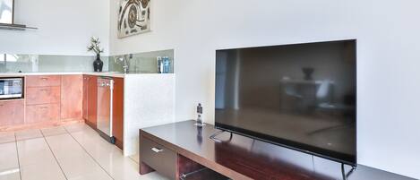 A modern kitchen with a flat-screen TV, wooden cabinets, and a tiled floor.