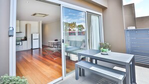 Un apartamento moderno con una puerta corrediza de vidrio que da a un balcón, una pequeña cocina y un comedor con mesa y banco.