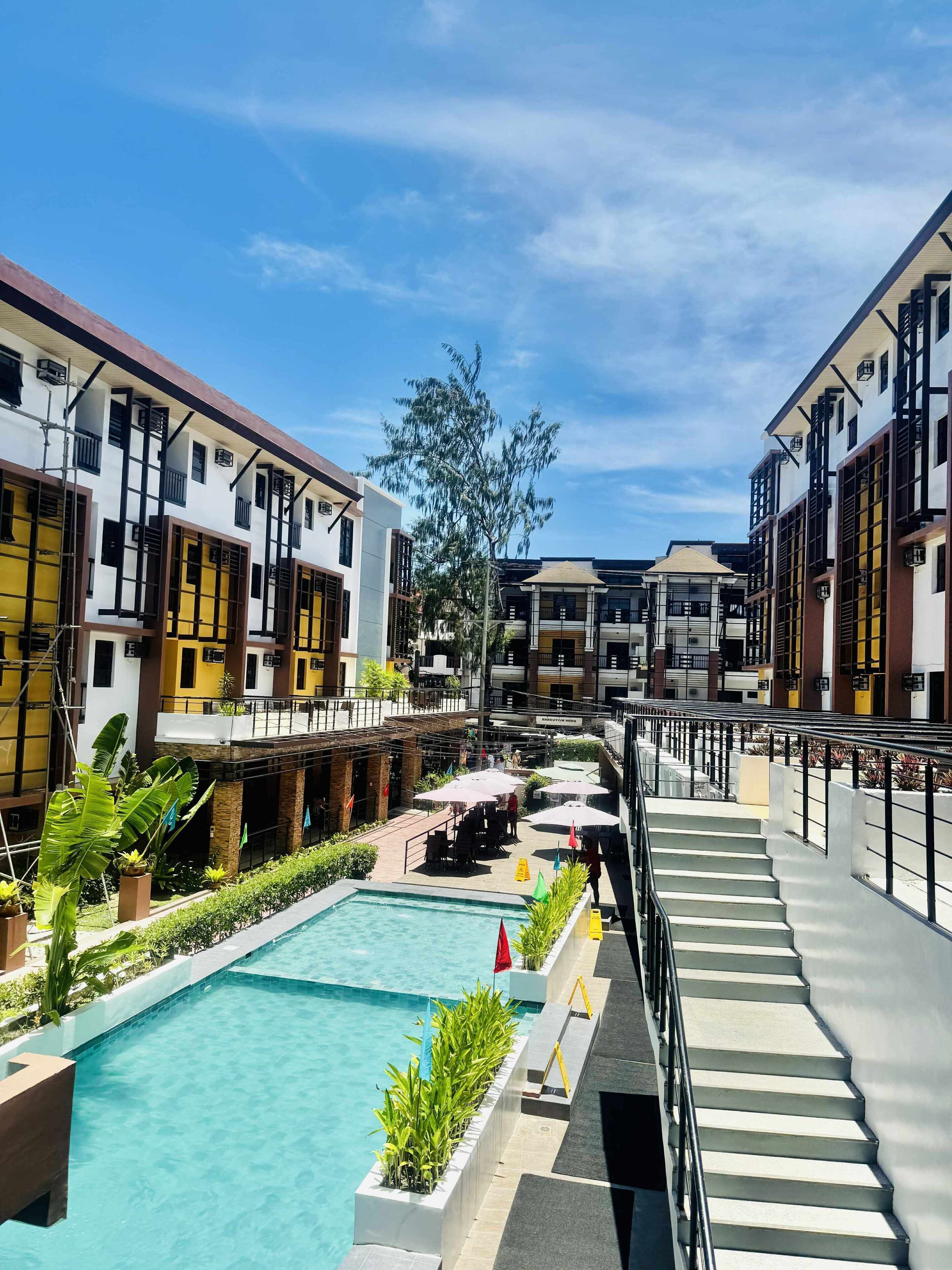 A modern hotel with a swimming pool, outdoor seating, and a staircase leading to upper floors.