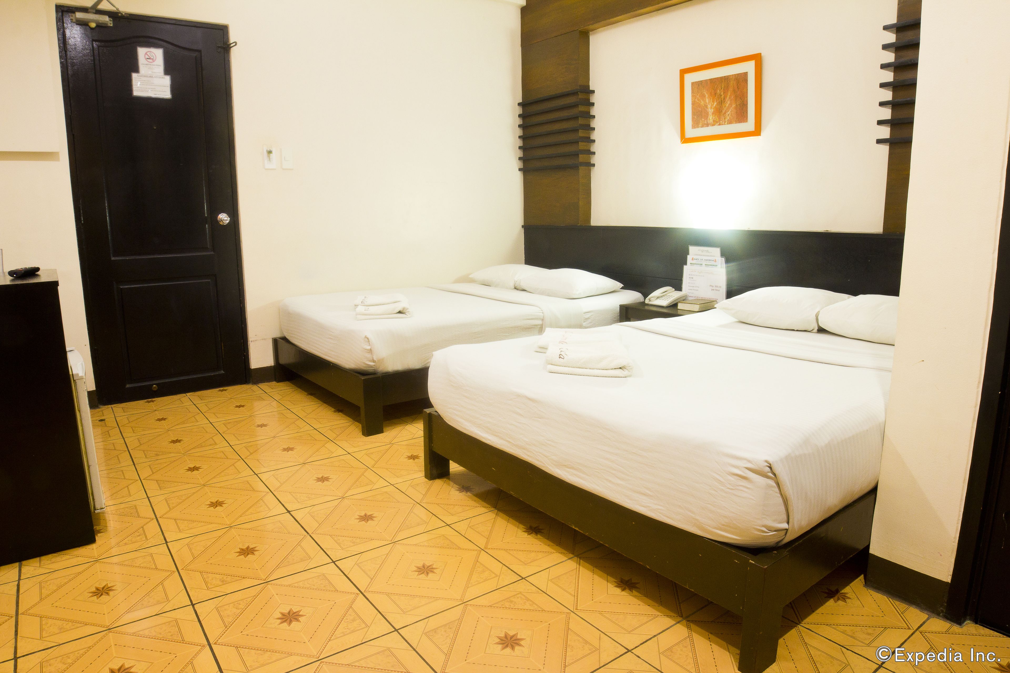 A hotel room with two beds, a black door, a framed picture on the wall, and a tiled floor.