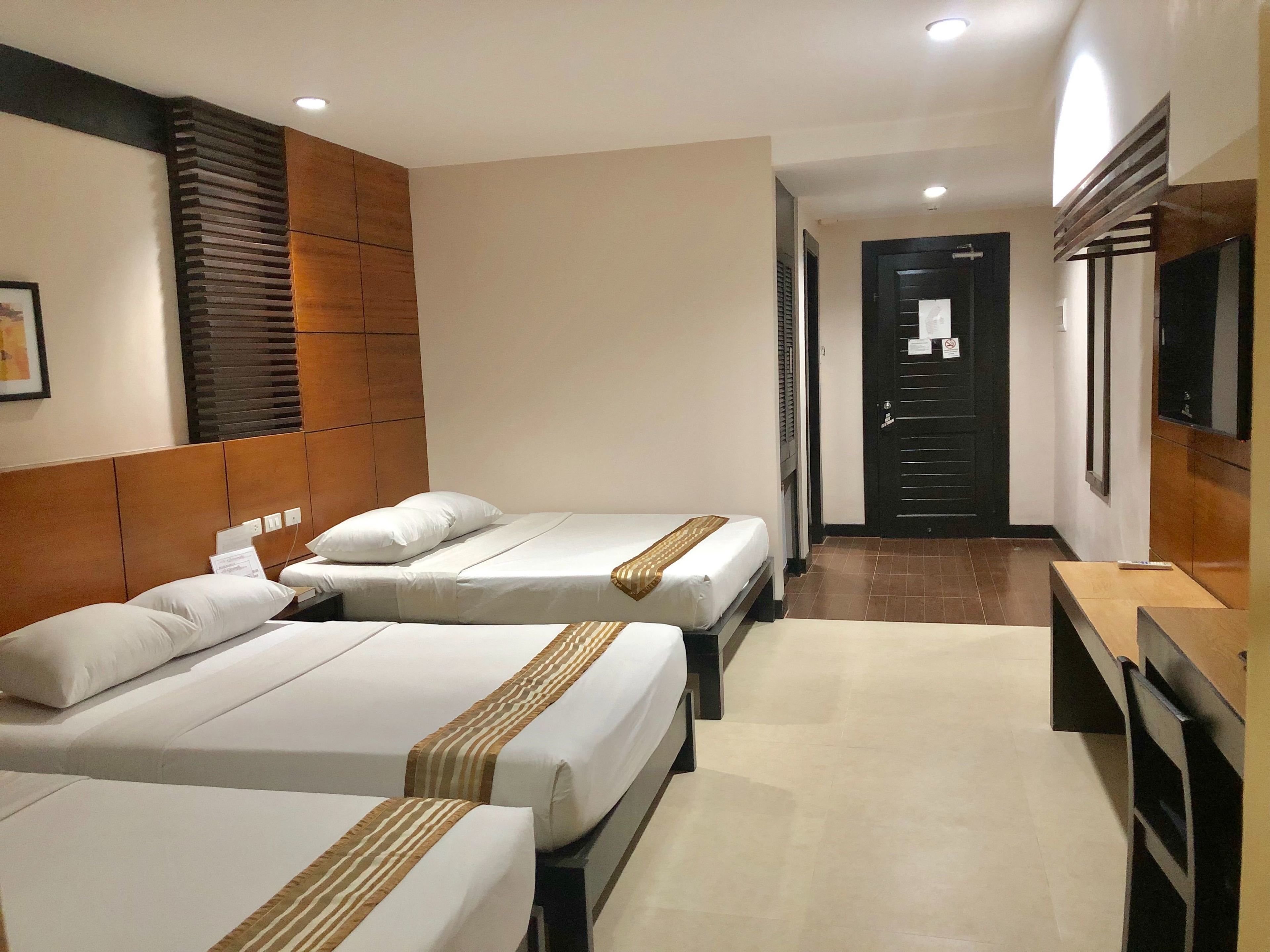 A hotel room with two beds, a wooden headboard, a flat-screen TV, and a desk with a chair.