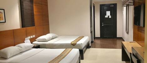 A hotel room with two beds, a wooden headboard, a flat-screen TV, and a desk with a chair.