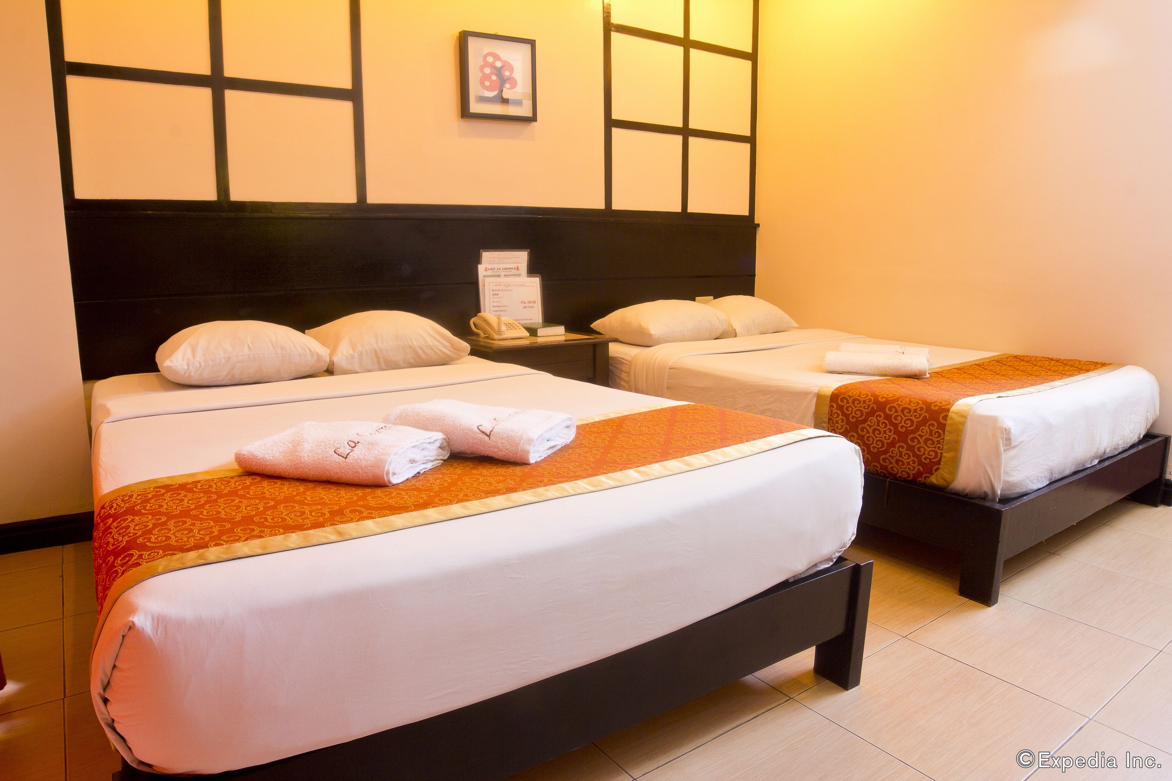 A hotel room with two beds, each with white linens and a brown headboard. There is a framed picture on the wall above the beds.