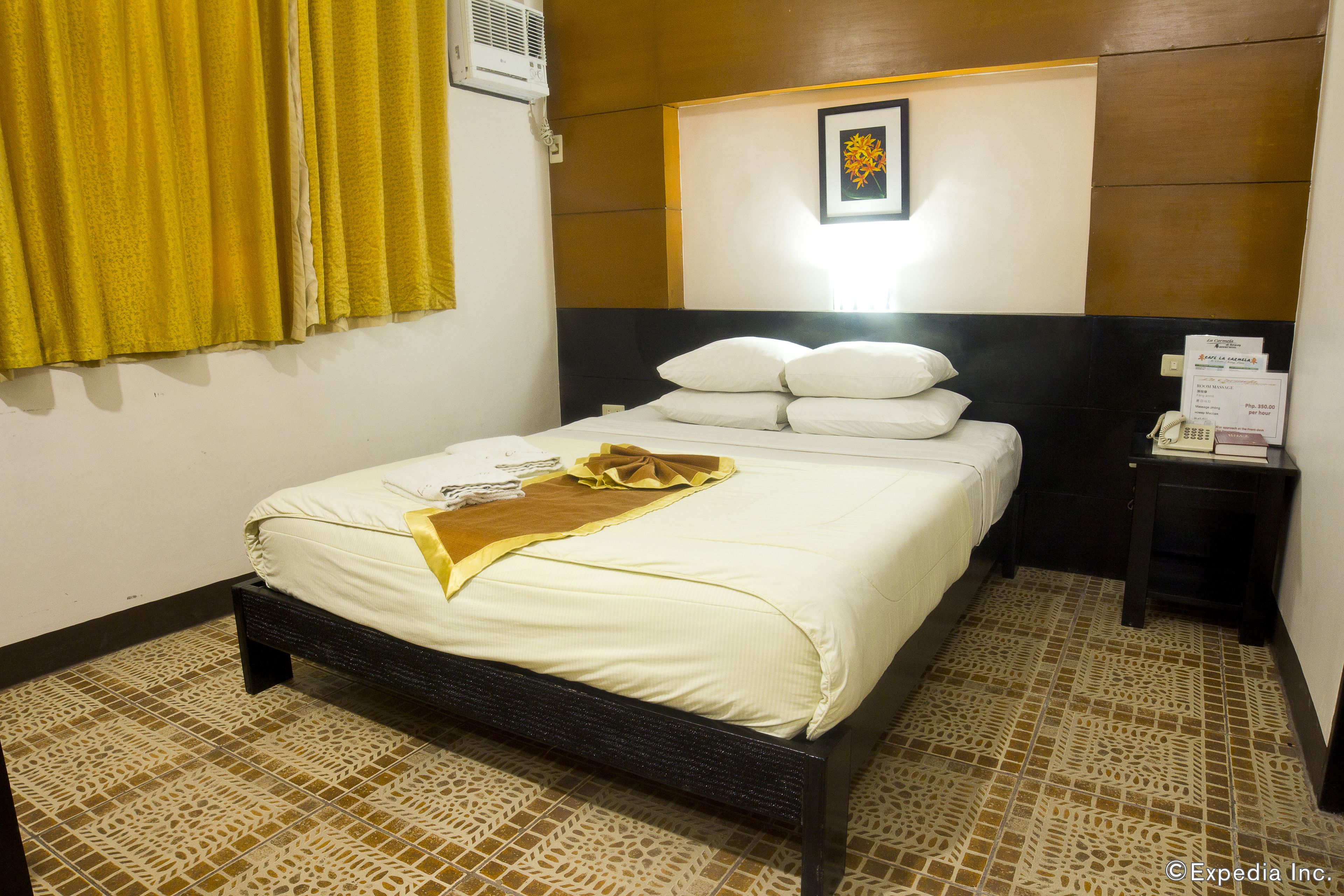 Habitación de hotel con cama, mesita de noche, un cuadro en la pared y ventana con cortinas amarillas.