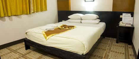 Une chambre d’hôtel avec un lit, une table de chevet, un tableau encadré au mur et une fenêtre avec des rideaux jaunes.