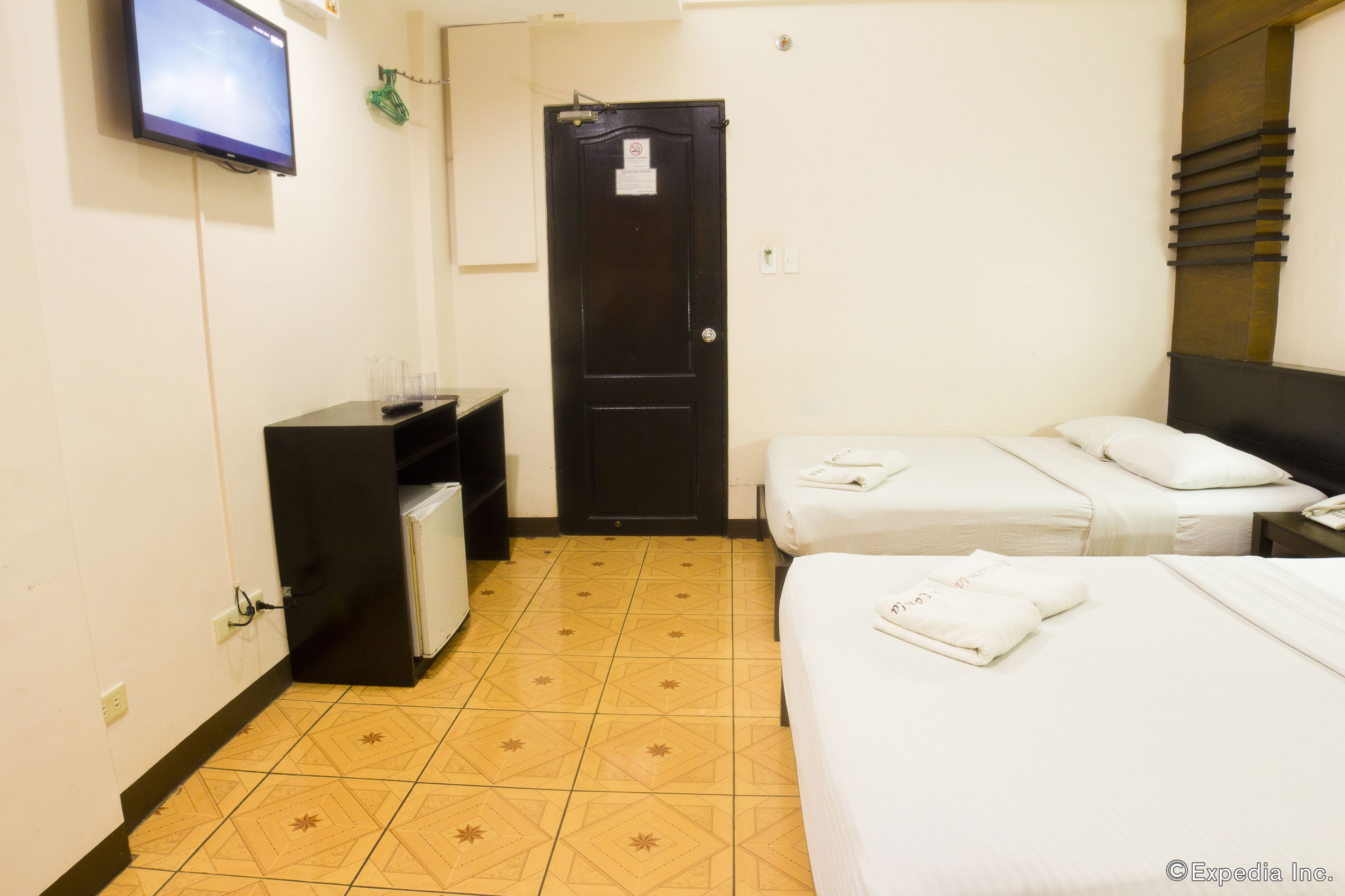 A hotel room with two beds, a TV mounted on the wall, a small desk, and a door with a sign.