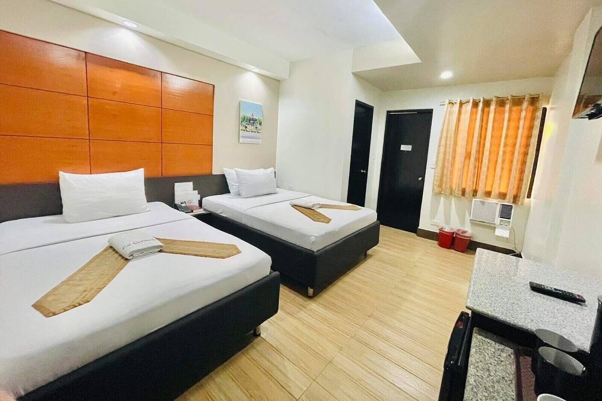 A hotel room with two beds, a desk, and a window with curtains.