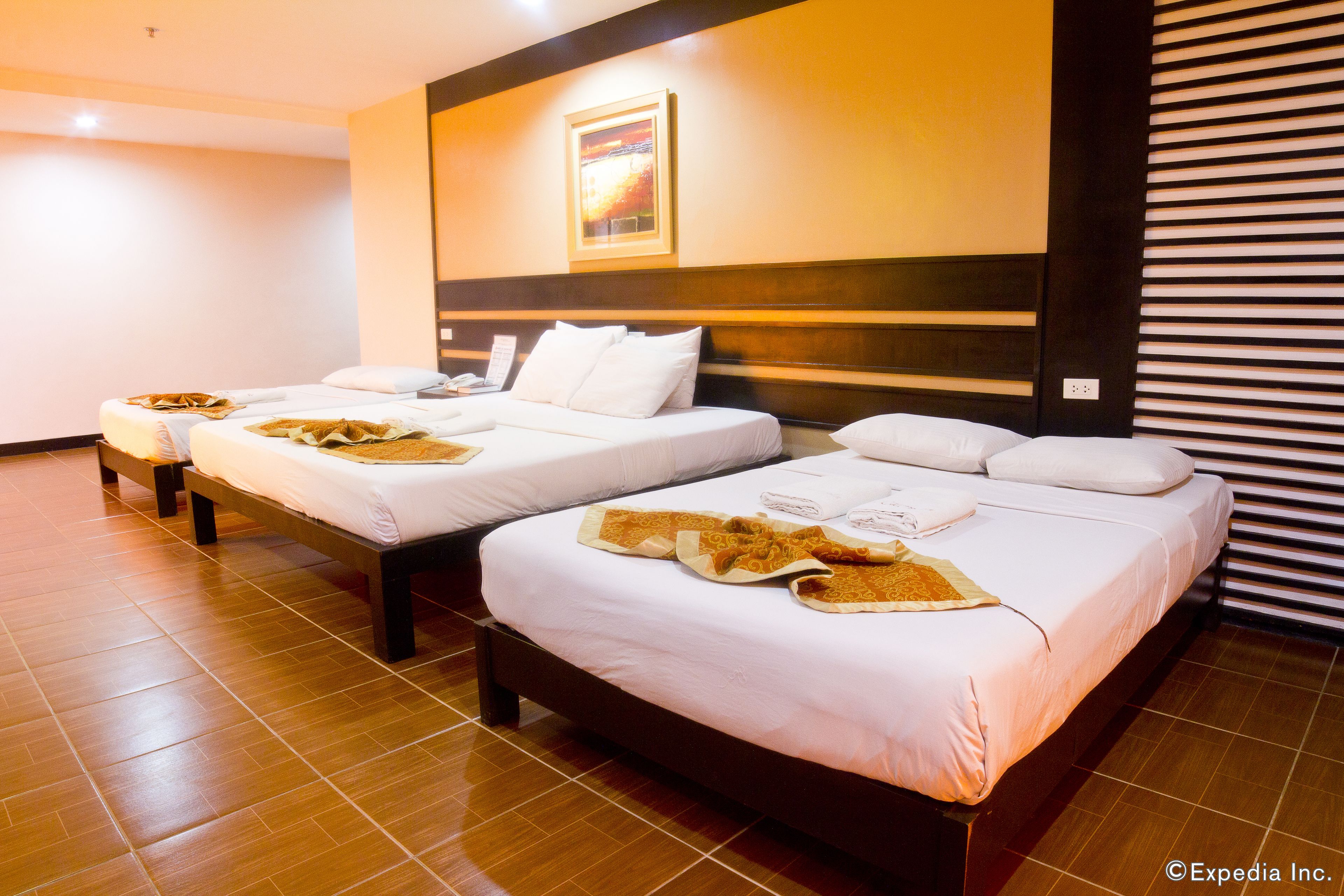 A hotel room with three beds, each with white linens and towels.