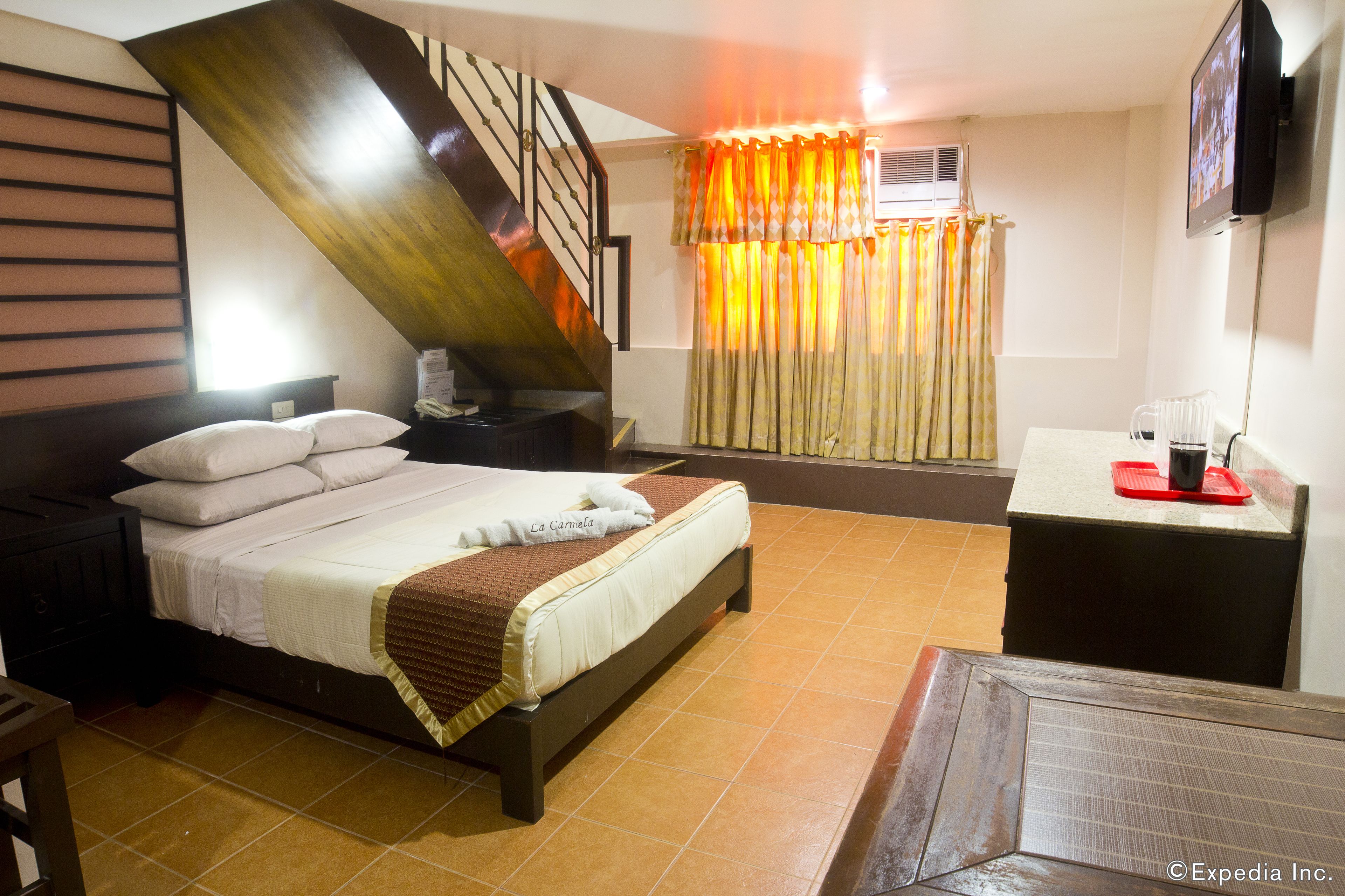 A hotel room with a bed, a desk, a TV, and a window with curtains.