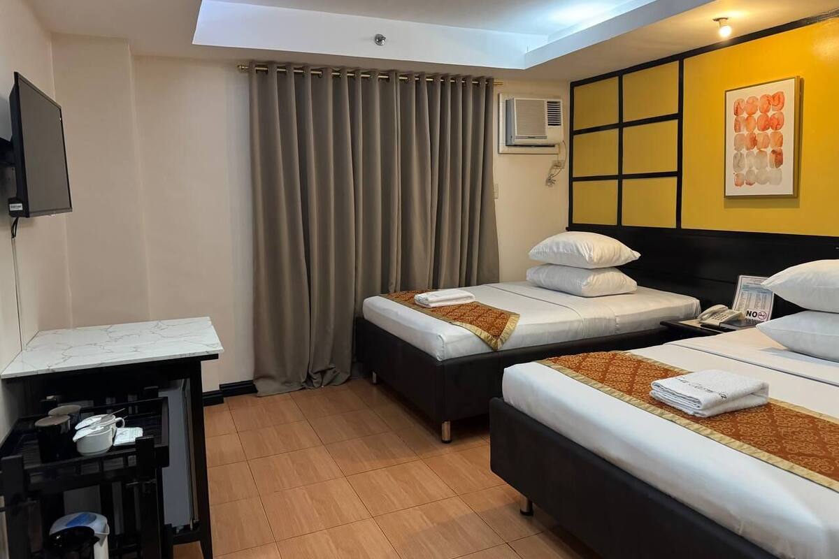 A hotel room with two beds, a desk, and a TV.