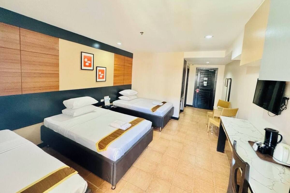 A hotel room with two single beds, a desk with a chair, a television, and a coffee maker.