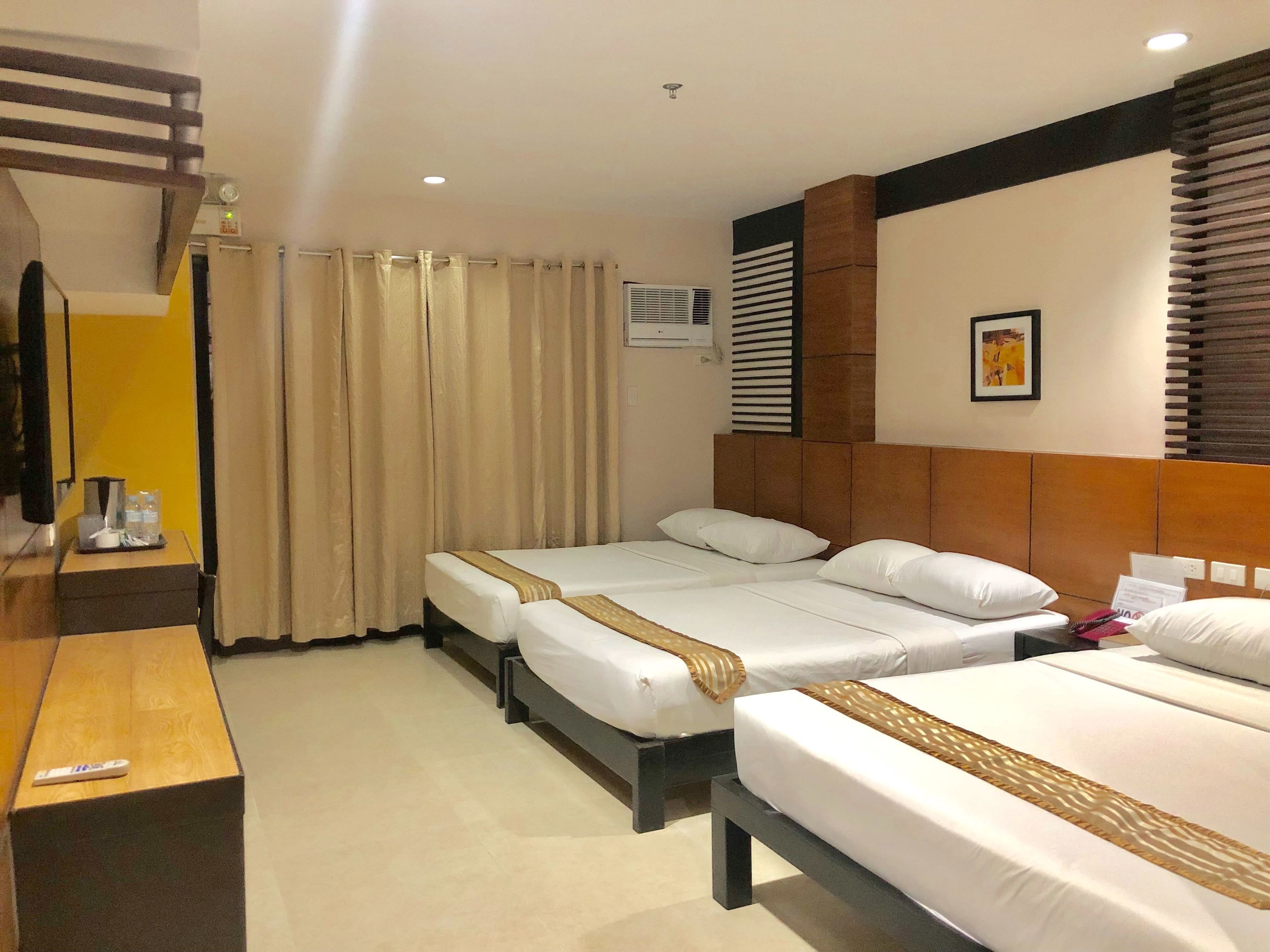 A hotel room with two beds, a wooden desk, a TV, and a window with blinds.