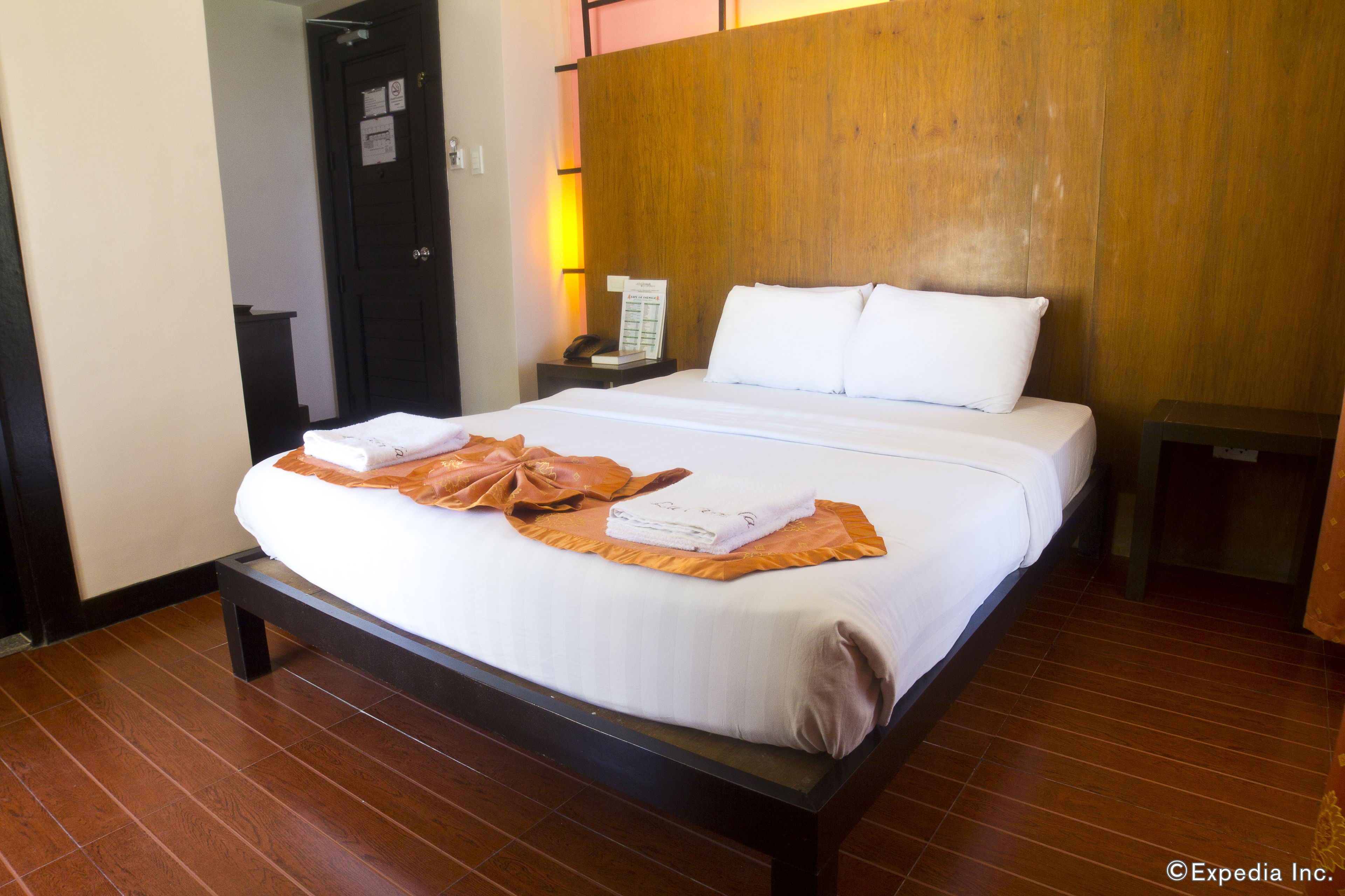 A hotel room with a large bed, wooden headboard, and a nightstand with a phone and a menu.