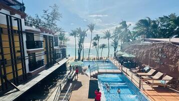 A pool area with a view of the beach, palm trees, and a building with a balcony.