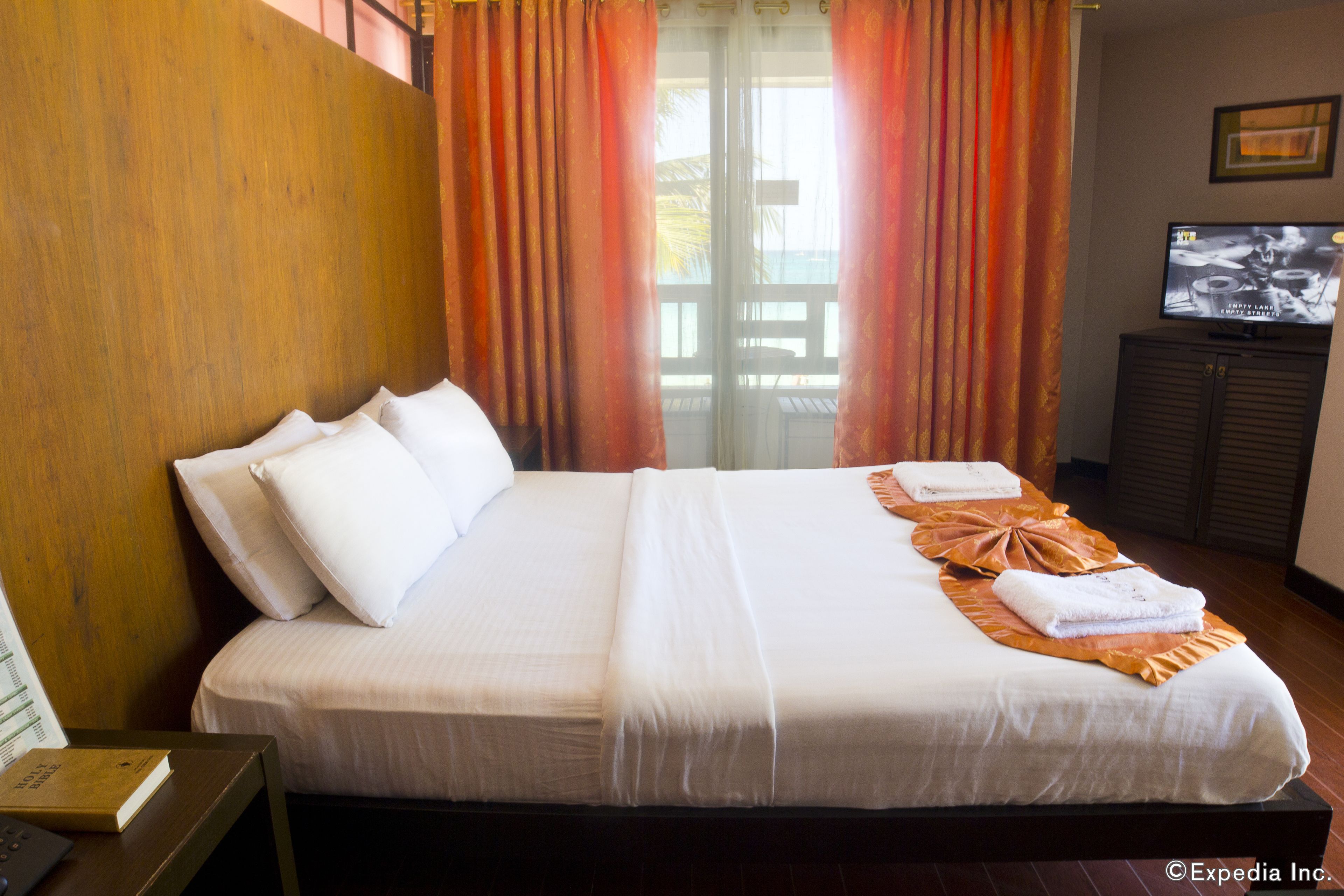 A hotel room with a large bed, a television, and a wooden headboard.