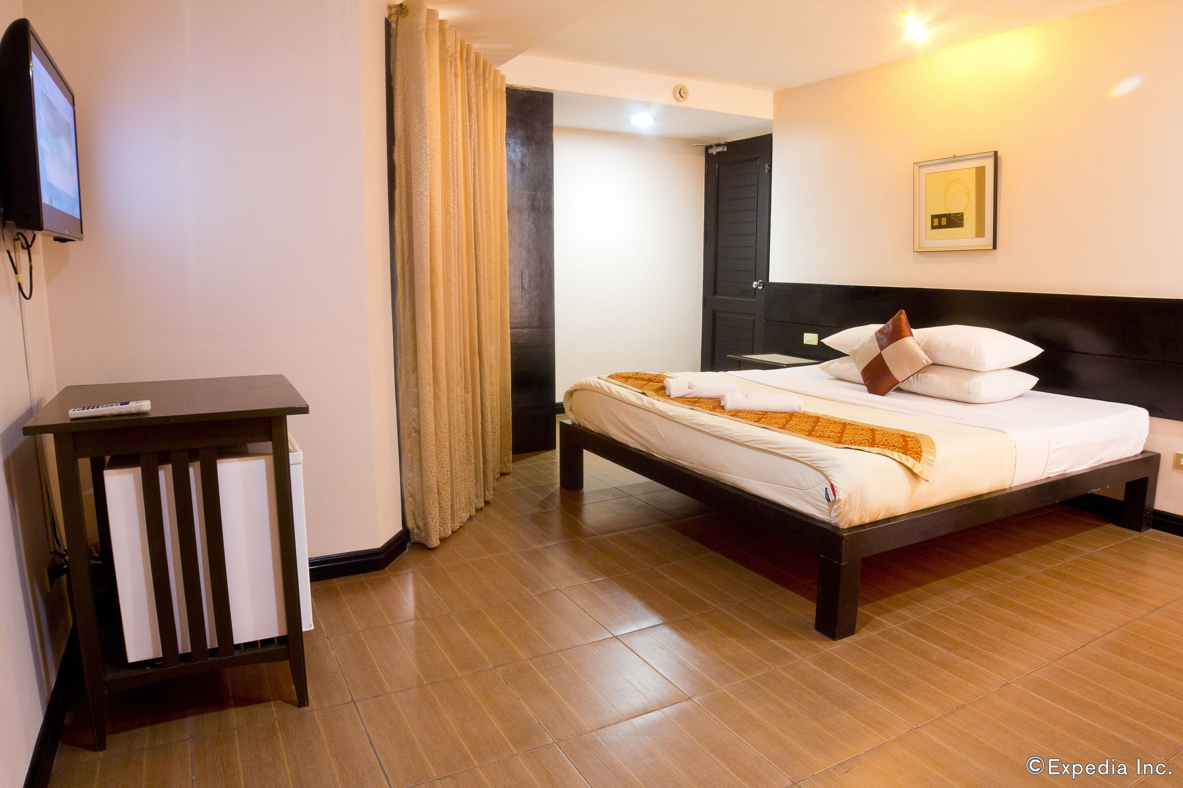 Una habitación de hotel con una cama, una mesita de noche, un televisor y una puerta que da a otra habitación.