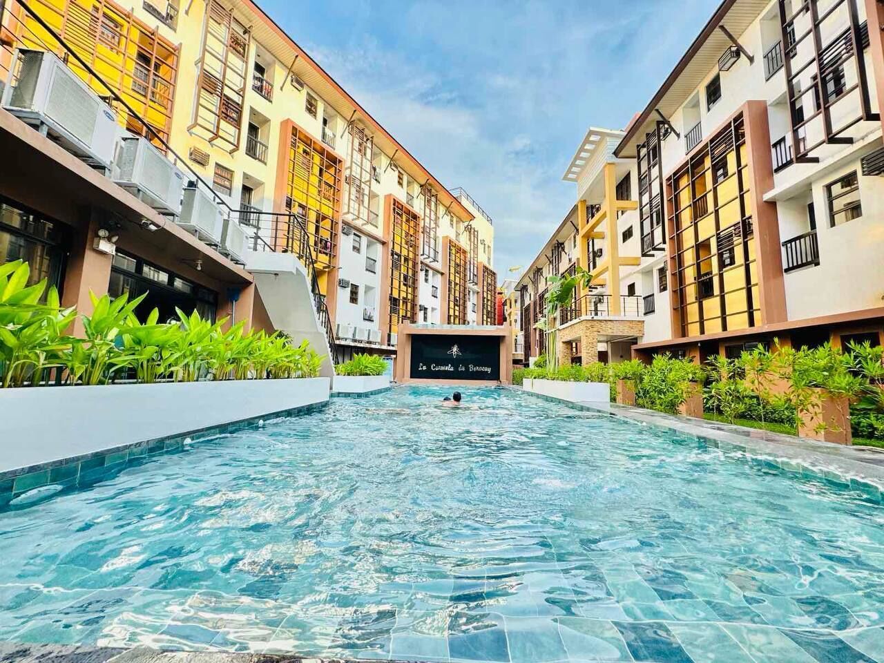 Una piscina con vistas a edificios altos, un cartel que dice "Le Comte de Boussy" y una persona nadando.