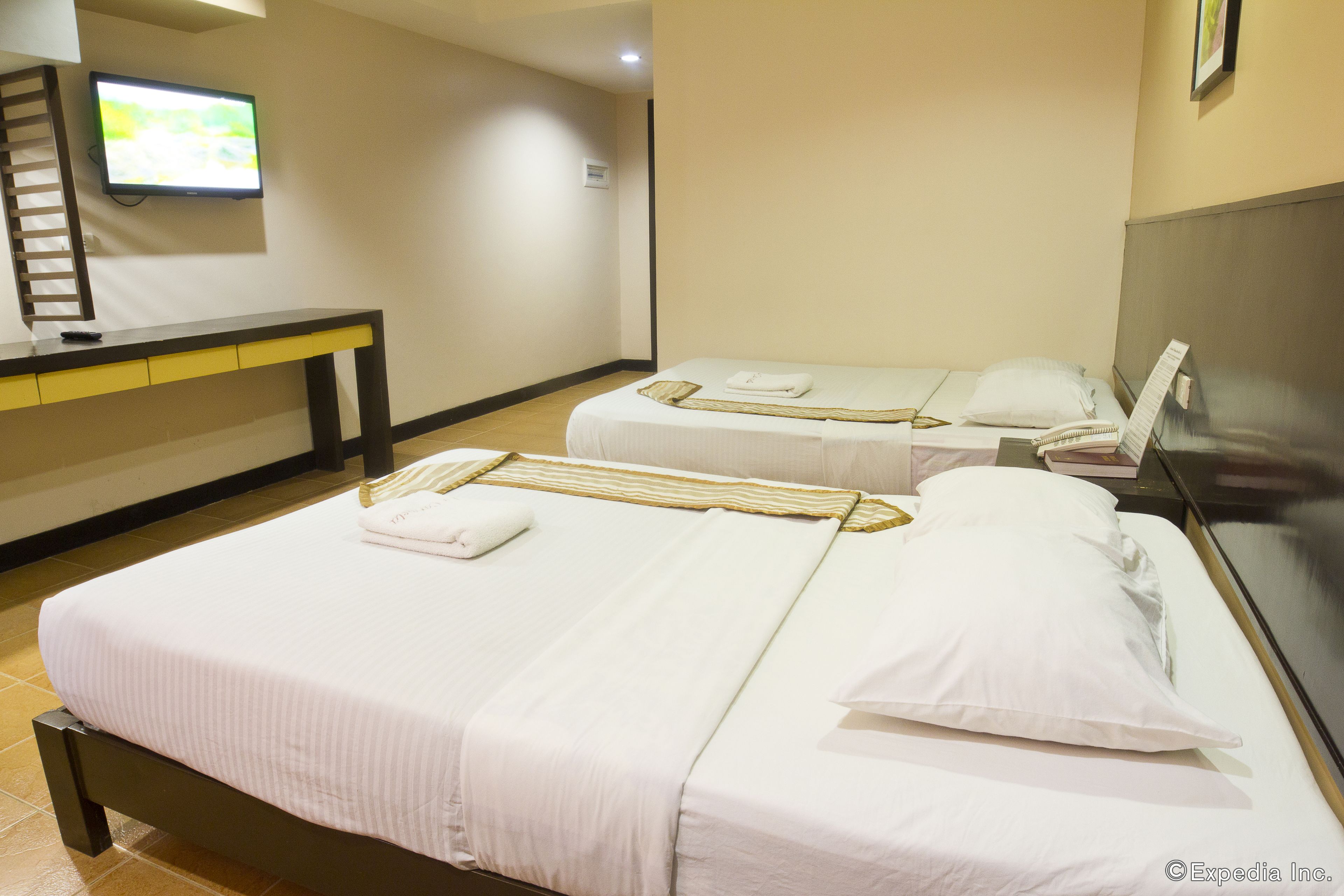 Habitación de hotel con dos camas, un televisor en la pared, un escritorio y un espejo.