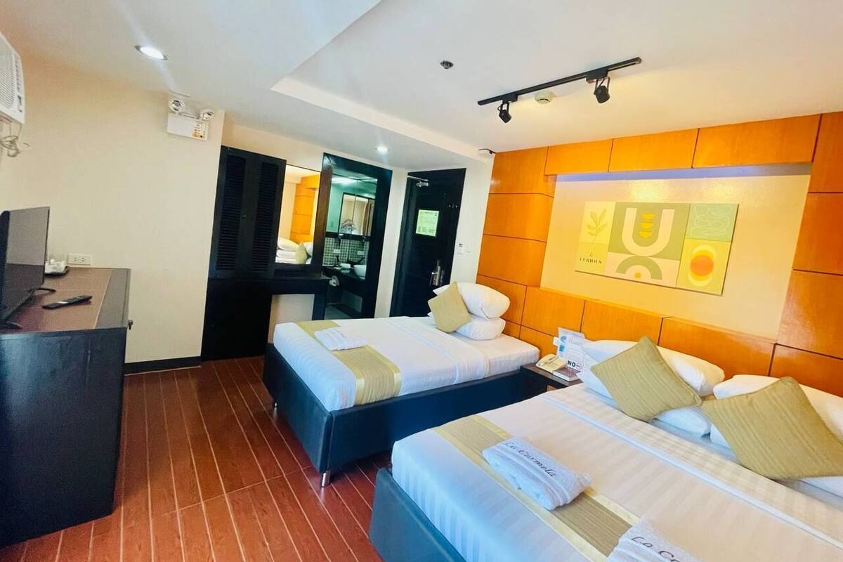A hotel room with two beds, a desk, and a bathroom visible through an open door.
