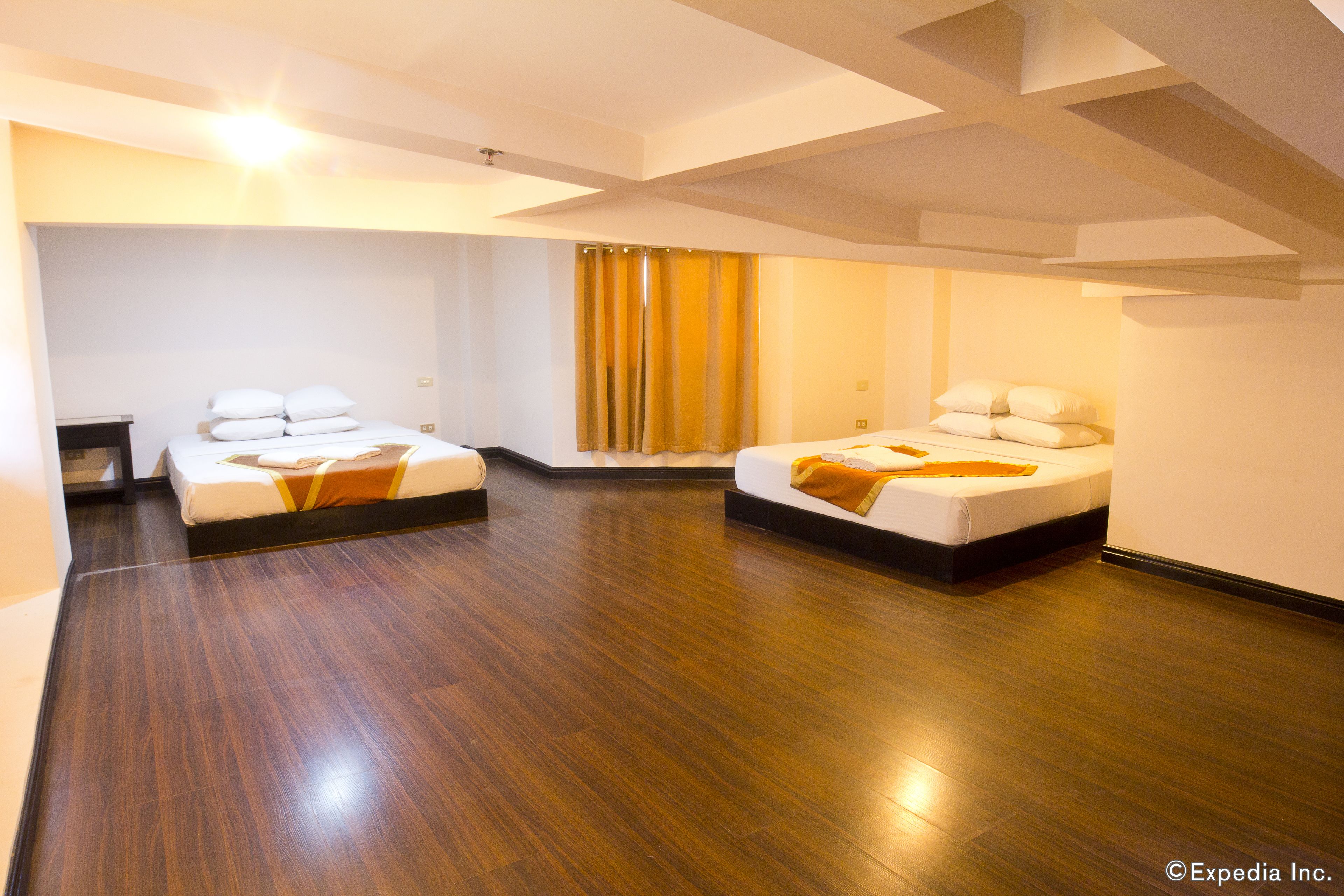 Een hotelkamer met twee bedden, houten vloeren en een groot raam met gordijnen.
