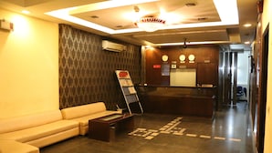 A hotel reception area with a reception desk, a waiting area with a sofa, a coffee table, and a patterned wall.