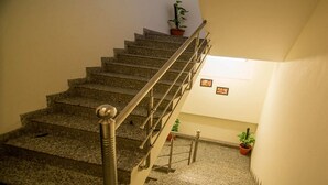 A staircase with granite steps and a metal handrail, leading to a landing with potted plants and framed pictures on the wall.