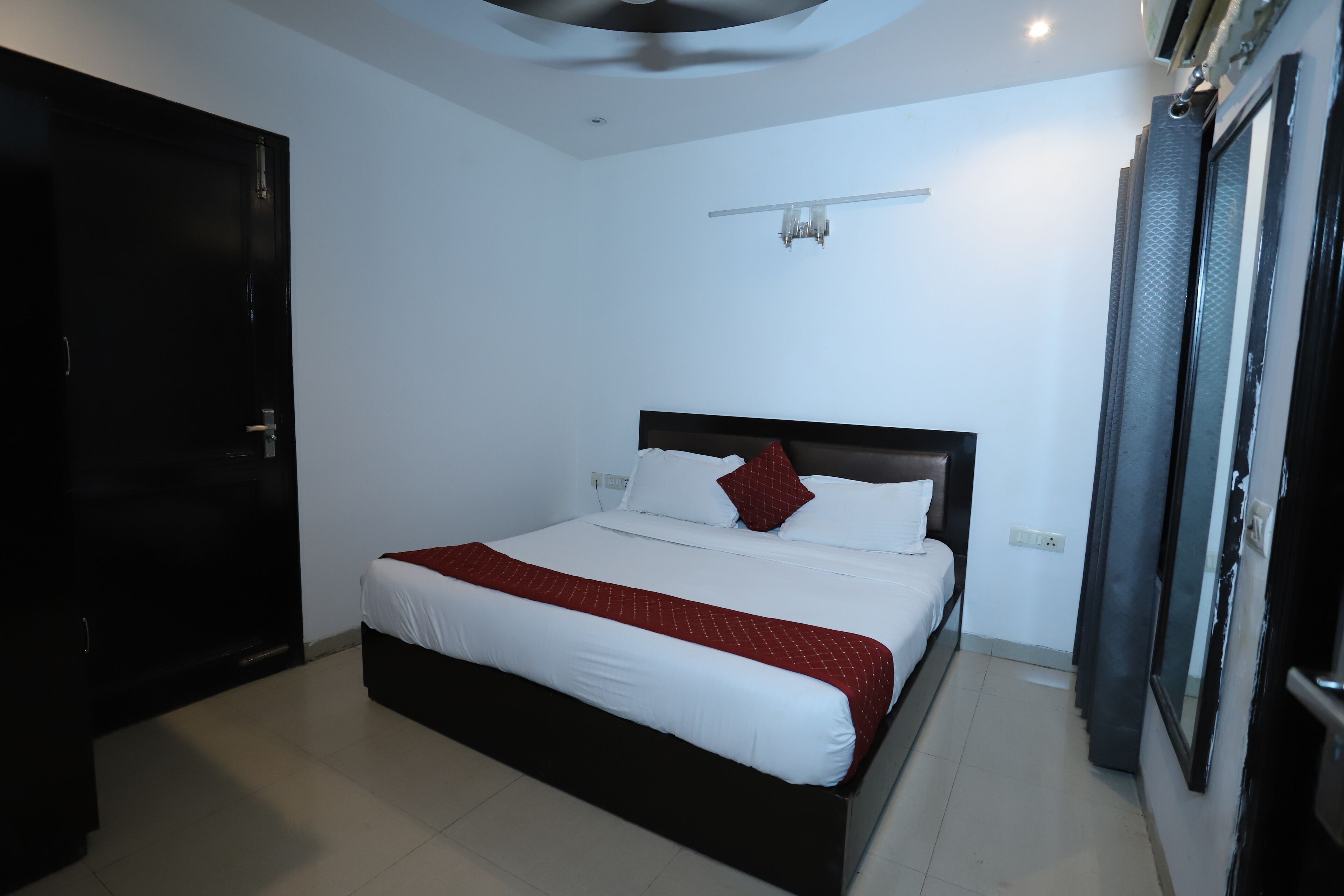 A hotel room with a bed, a door, a light fixture, and a window.