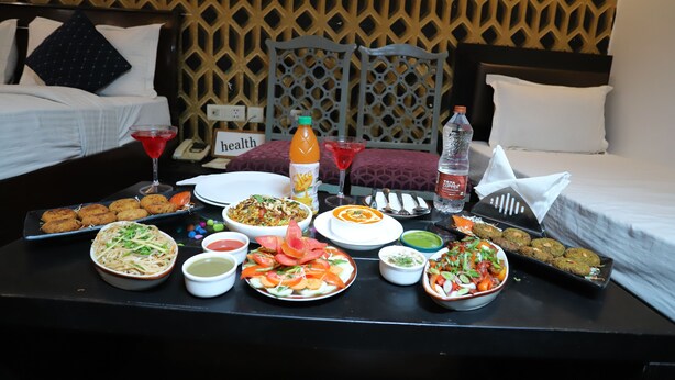 A dining table with various dishes, a bottle of orange juice, and a glass of red drink in a hotel room.